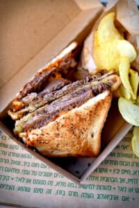 כריך עם פרוסות רוסטביף על לחם קלוי עם צ'יפס בקופסת טייק-אווי חומה.