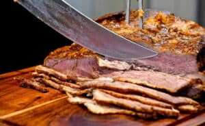 סכין גדולה חותכת חזה בקר עסיסי ומבושל על קרש חיתוך מעץ.