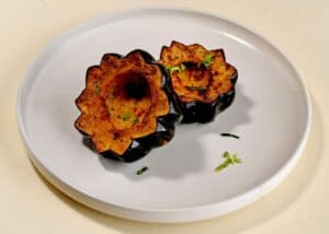 שני חצאי דלעת אקורן צלויים עם עשבי תיבול על צלחת לבנה, מונחים על משטח בהיר.