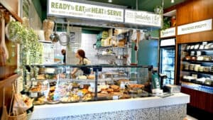 דלפק מעדנייה עם מאפים ומנות שונות, עובד מאחורי הזכוכית ומדפים עם מזון ארוז.