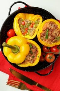 פלפלים צהובים ממולאים באורז וירקות על צלחת שחורה עם עגבניות שרי וסכו"ם.