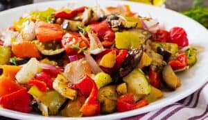 רטטוי צבעוני עם ירקות קלויים כמו פלפלים, עגבניות, חצילים ובצלים על צלחת לבנה.