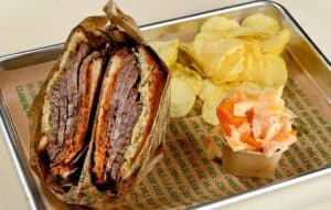 כריך רוסטביף עם צ'יפס ותוספת של סלט כרוב על מגש מתכת מרופד בנייר חום.