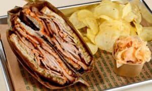 כריך בשר עבה עם צ'יפס וכוס קטנה של סלט כרוב על מגש.