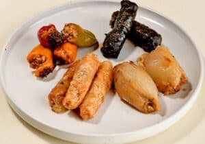 צלחת לבנה עם עלי גפן ממולאים, פלפלים ממולאים וכרוב ממולא מסודרים בצורה מסודרת.