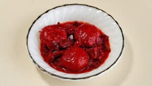 שלוש כופתאות אדומות ועגולות בקערה לבנה עם רוטב אדום וירקות חתוכים לקוביות.