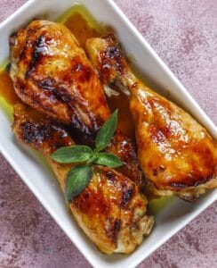 שלוש כרעי עוף מזוגגות ברוטב, מעוטרות בבזיליקום טרי, מוגשות בצלחת לבנה.